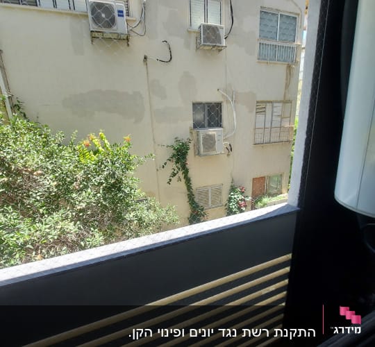 רשת יונים על חלון עם מזגנים על קיר חיצוני
